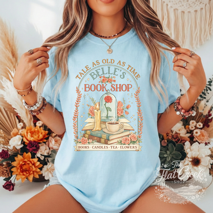 Light blue t-shirt with 'Belle's Book Shop' design worn by a person, surrounded by flowers and decorative elements.