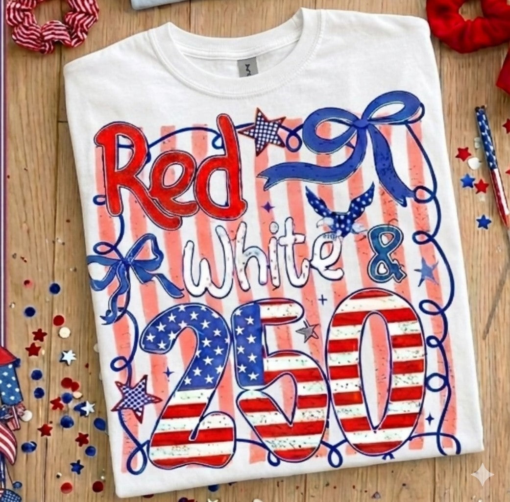 White t-shirt with red, white, and blue design on a wooden surface with festive decorations.