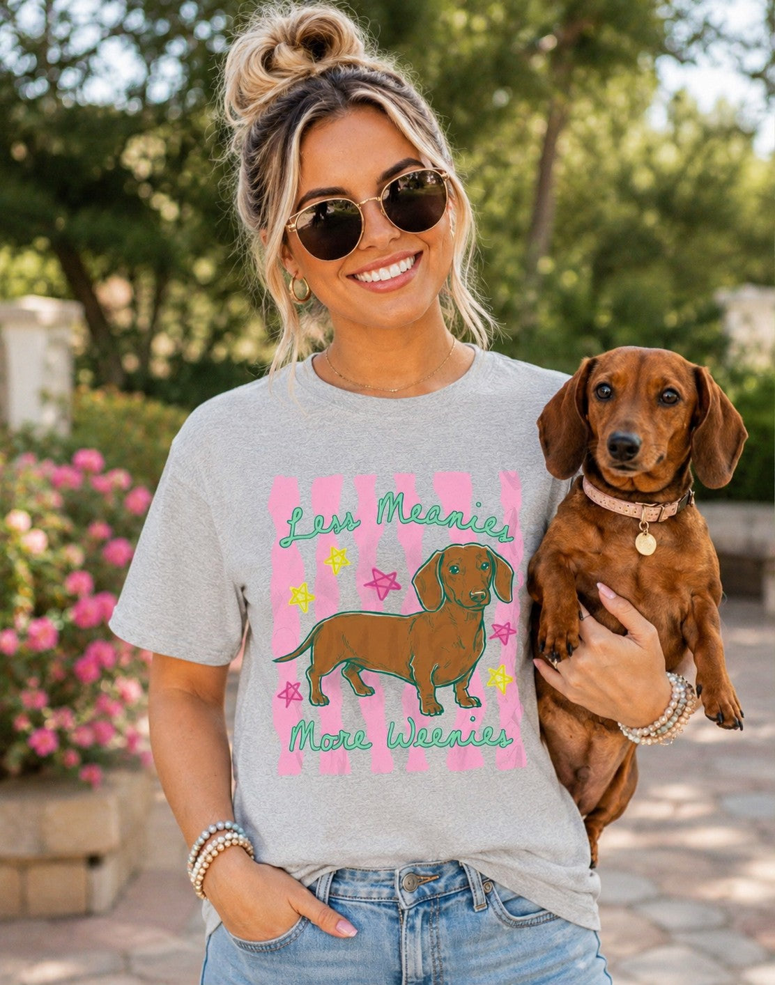 Woman holding a dachshund wearing a t-shirt with a dog graphic and text.