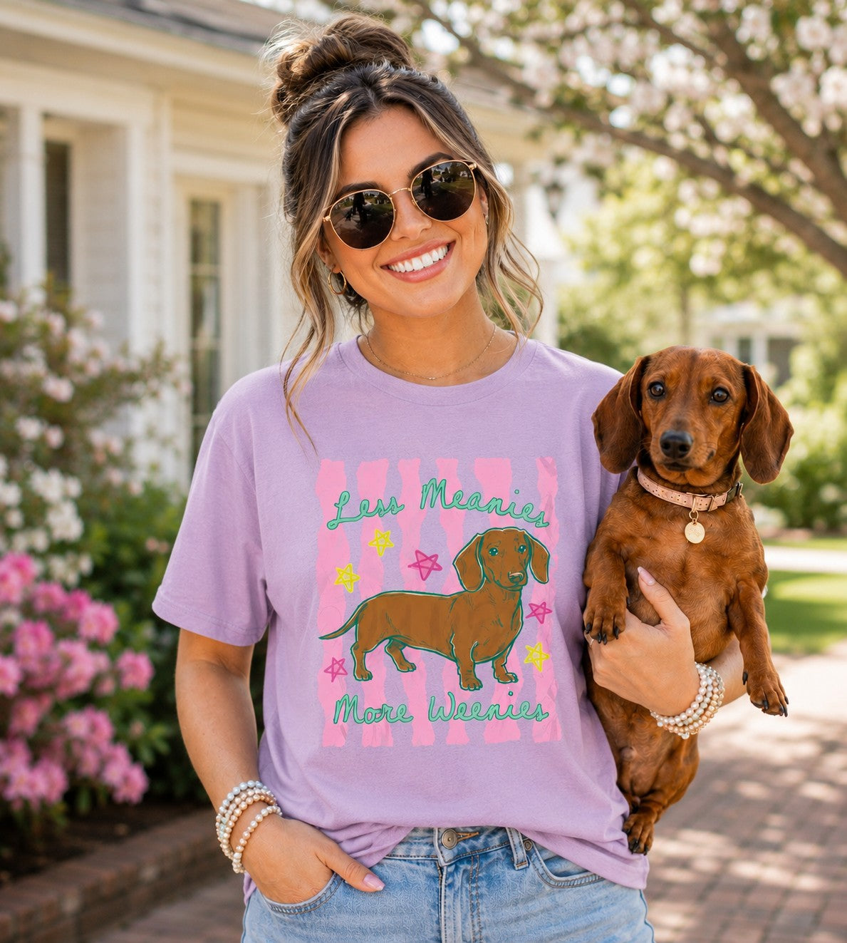 Woman wearing a purple t-shirt with a dog graphic and text, holding a small brown dog outdoors.