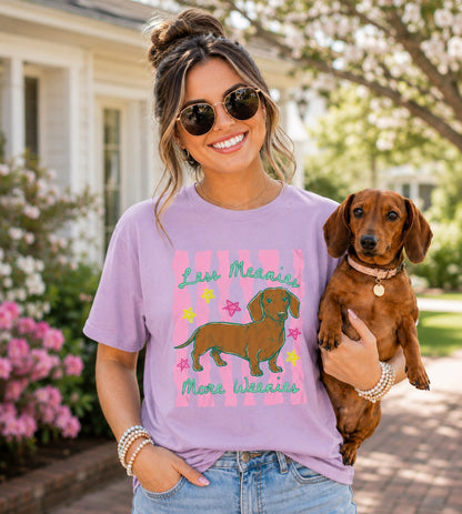 Woman wearing a purple t-shirt with a dog graphic and text, holding a small brown dog outdoors.